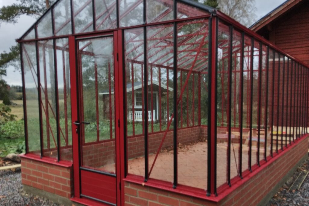 Växthus i röd färg med glasdörr och glasfönster